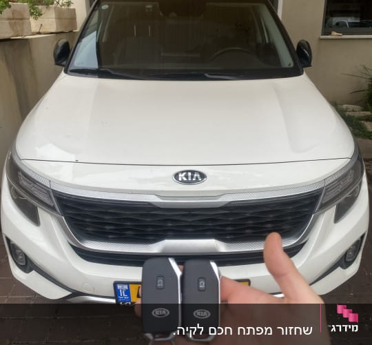 מפתחות רכב קיה מוחזקים מול רכב לבן
